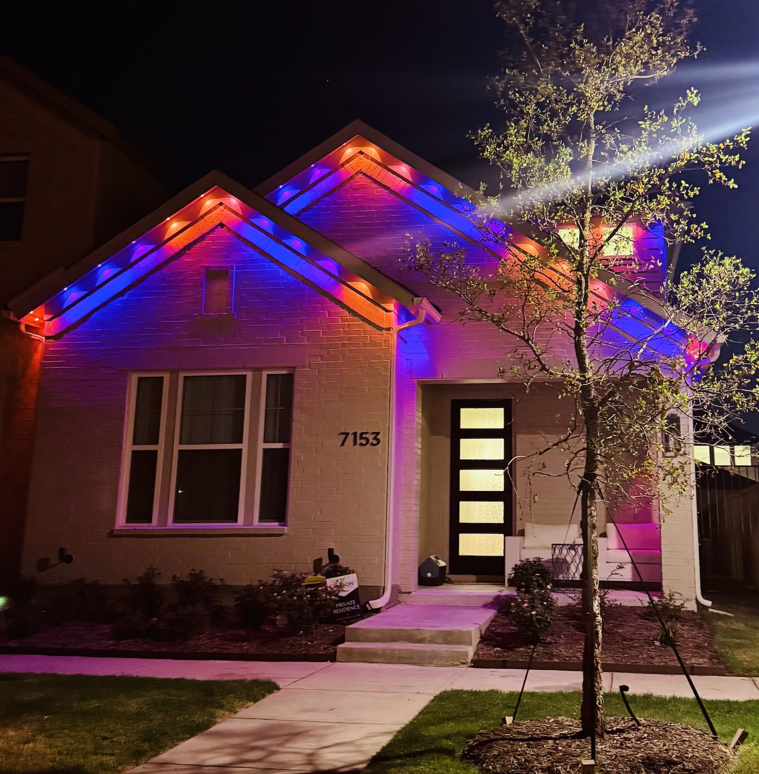 Brick home with purple and orange permanent gable lighting at night