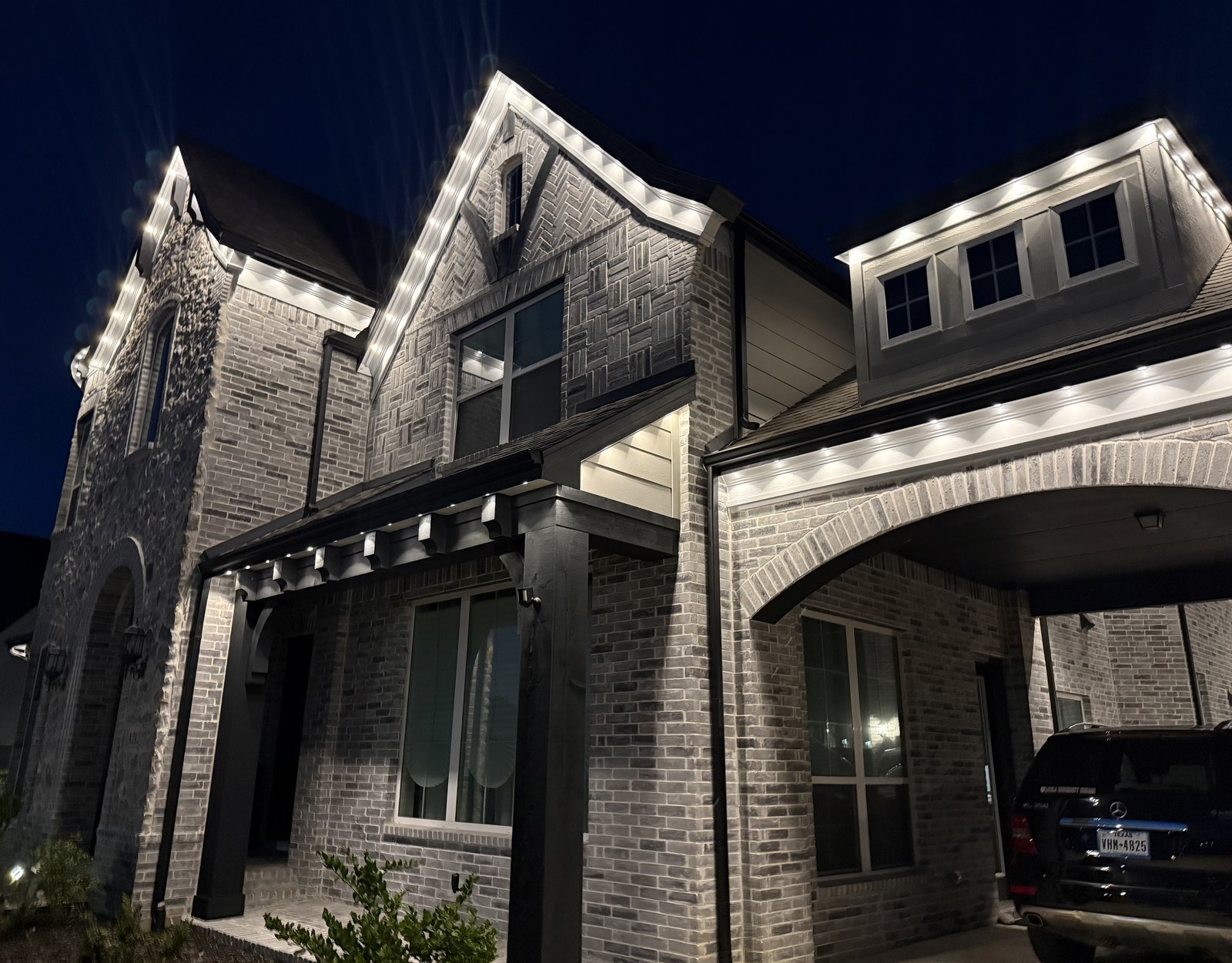 Two-story Tudor brick home with crisp warm white permanent roofline and eave lighting at night in Texas
