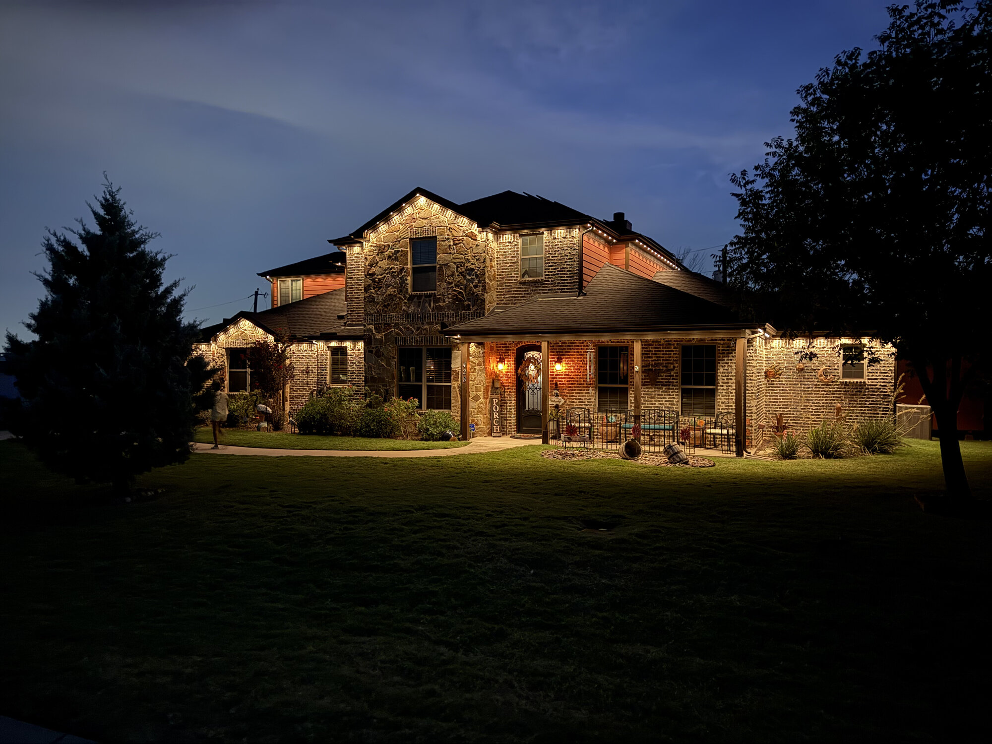 Two-story stone and brick home with warm white permanent lighting at dusk