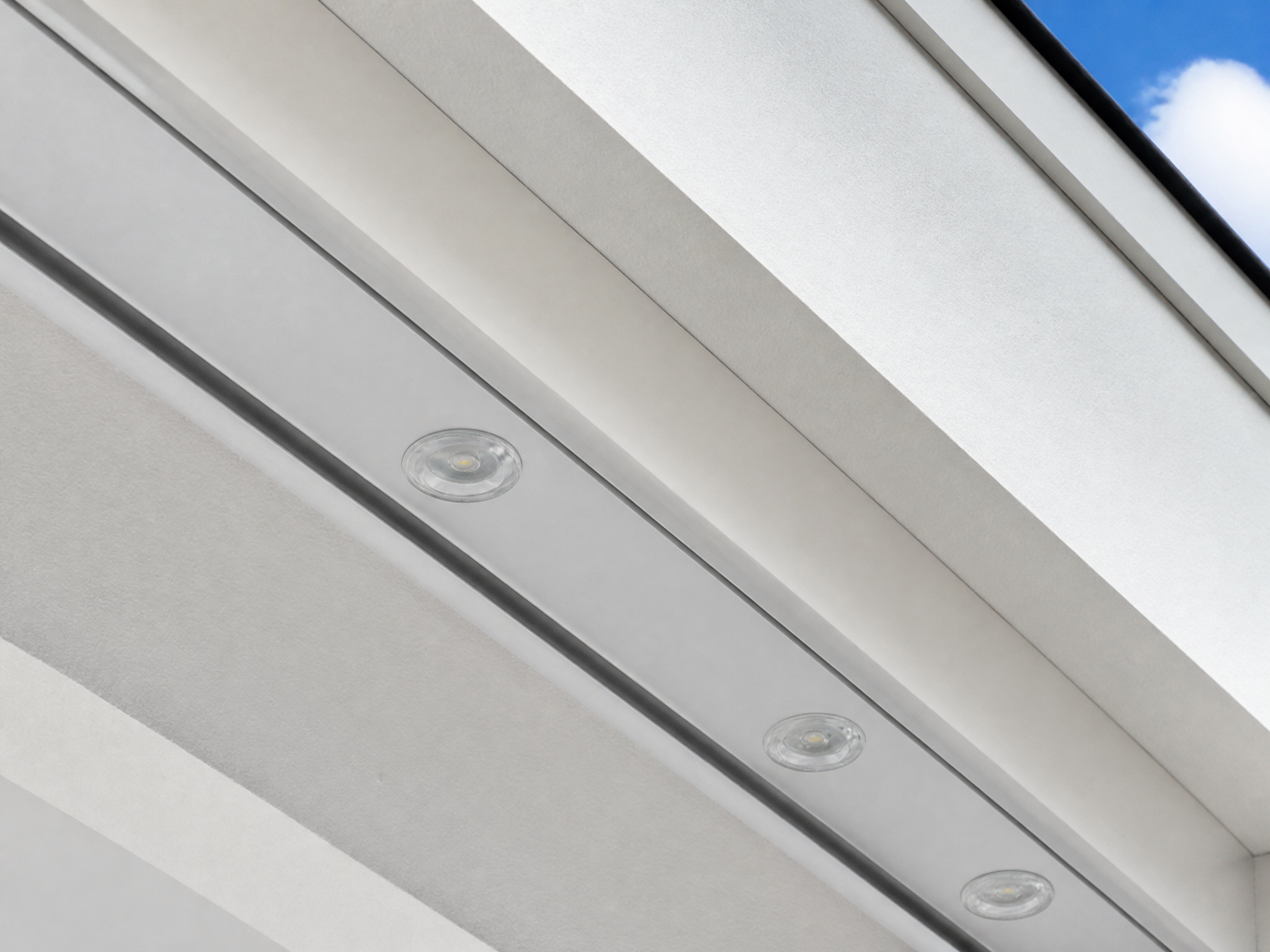 Close-up of a slim white powder-coated aluminum lighting channel mounted under a white soffit, with small downward-facing LED lenses inside the track